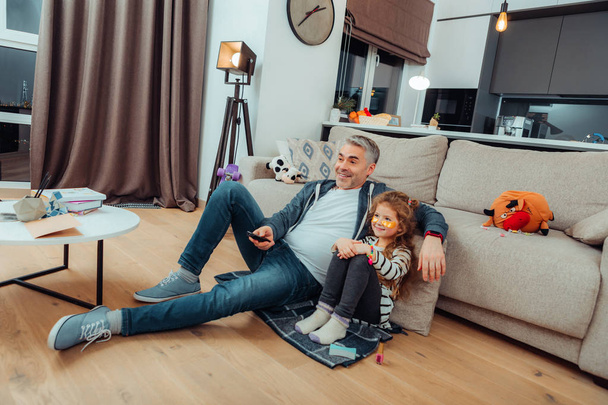 Pretty small daughter in a striped sweater and her father sitting on the floor - Fotoğraf, Görsel
