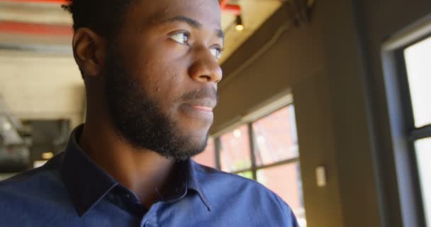 Vista frontal do jovem empresário negro feliz olhando para a câmera em um escritório moderno. Empresário atencioso olhando para longe 4k
 - Filmagem, Vídeo