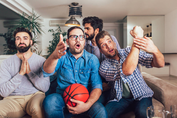Amis heureux ou fans de basket regarder le match de basket-ball à la télévision et célébrer la victoire à la maison.Concept d'amitié, de sport et de divertissement
. - Photo, image