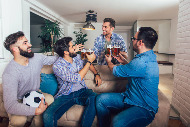 Amis masculins regardant la télévision et acclamant des jeux de sport sur le canapé à la maison. Groupe d'amis regardant le match de football américain
. - Photo, image