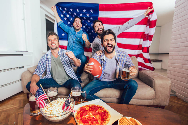 männliche Freunde fernsehen und auf dem heimischen Sofa Sportspiele bejubeln. Gruppe von Freunden schaut American Football Spiel. - Foto, Bild