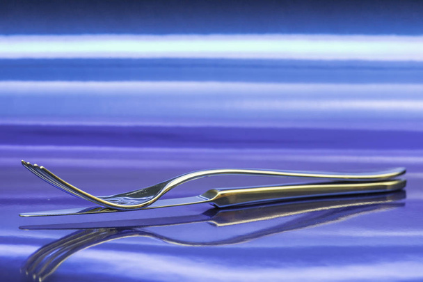 tenedor y cuchillo sobre una superficie metálica que refleja su figura invertida, todo en el azul
 - Foto, imagen