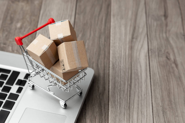 Delivery of the order from the online store. Online shopping. Boxes with goods in the shopping basket on the table with laptop. Copy space for text. - 写真・画像