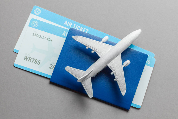 Bilhetes para avião e passaporte com modelo de avião de passageiros em fundo cinza
 - Foto, Imagem