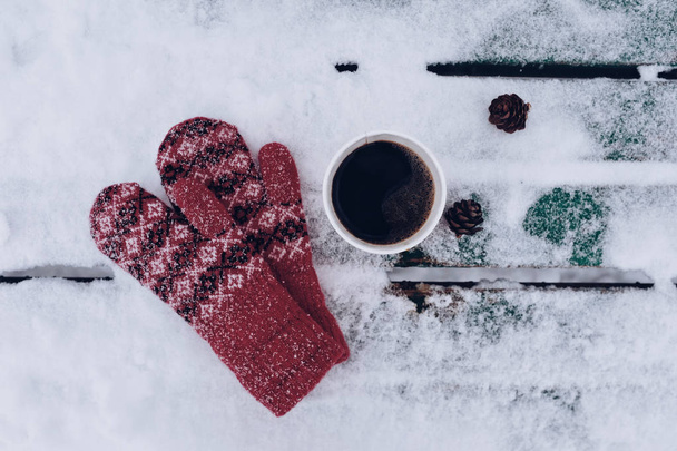 Winter concept - cup of hot coffee and warm red mittens in snowy wooden background - Foto, Imagen