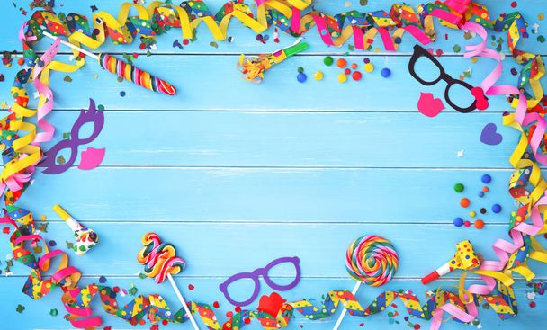 Colorful carnival or birthday background with streamers, confetti and other party accessoires on blue wooden planks - Фото, изображение