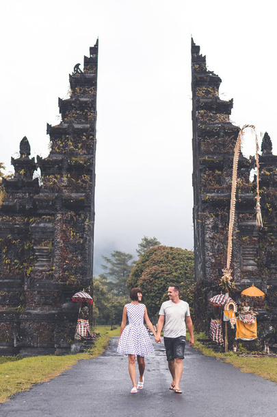 Joven pareja de luna de miel en un gran fondo de puertas balinesas. Isla de Bali, Indonesia
. - Foto, Imagen