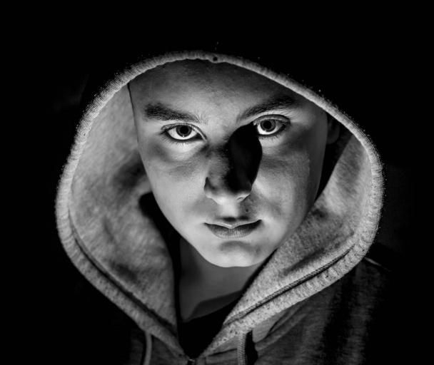 Stylish portrait of handsome caucasian young boy in the hood. Black and white shot, low key lighting. Isolated on black. - Foto, Imagen