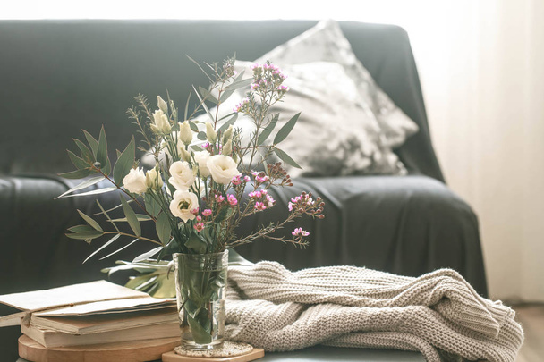 Acogedora sala de estar interior de la casa con un sofá negro y un jarrón con flores y artículos de decoración en una pequeña mesa
 - Foto, imagen
