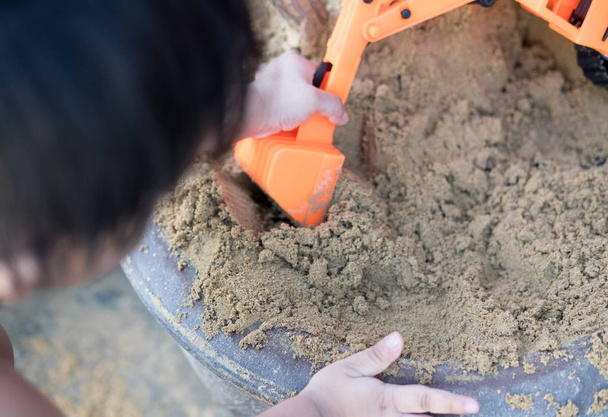 Junge spielt orangefarbenen Spielzeuglader auf Sandkasten auf Hof - Foto, Bild
