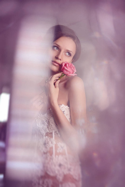 Fashion Bride. Young beautiful model girl with perfect skin and makeup, wedding dress with rhinestones and lace, flowers her hair. glass lamp glare. Soft focus, toning - Photo, Image