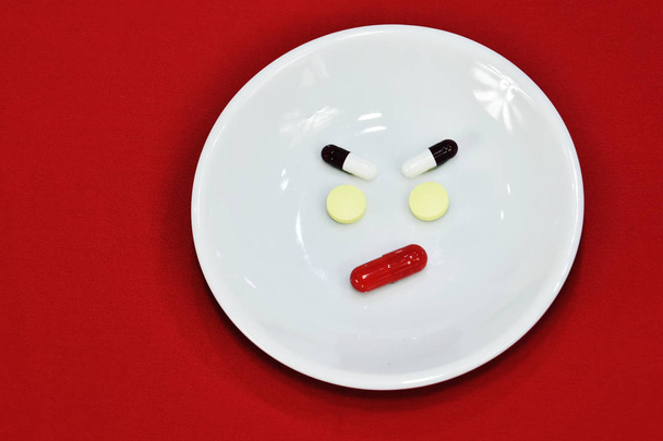 Sad face expression made of medicine. pain medication tablets. colored pills on porcelain dish. Assorted pharmaceutical pills. - Photo, image