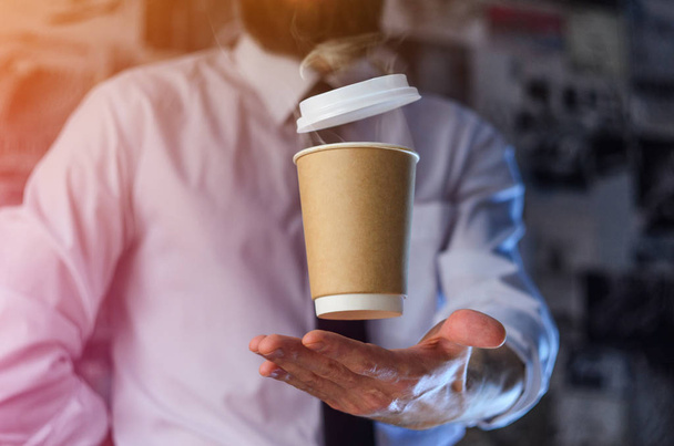 Barista in a white shirt with a tie holds floating in the air a paper cup with a hot drink on his outstretched arms. Barista wizard concept. Background for advertising and placing logo on your drink - Fotoğraf, Görsel