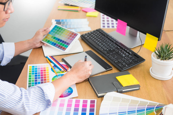 designer Editor no trabalho desenho esboça um novo projeto em tablet gráfico e paleta de cores sentado na mesa com computador em estúdio ou escritório
 - Foto, Imagem