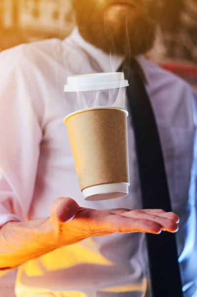 Barista in a white shirt with a tie holds floating in the air a paper cup with a hot drink on his outstretched arms. Barista wizard concept. Background for advertising and placing logo on your drink - 写真・画像