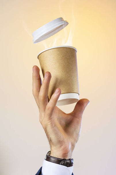 Hand of a business man in a blue jacket, white shirt and watch catches a flying cup of hot coffee with steam from a drink. Coffee break advertising concept. Empty place for your logo placement. - Foto, imagen