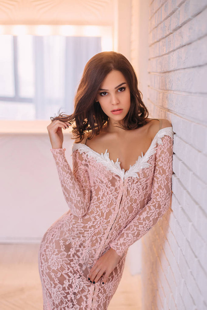 Luxurious brunette girl, with a bob haircut, posing in an expensive, pink dress with an open back. The princess in the white room. Scandinavian minimalist style interior. Image for prom and party - Foto, Imagem