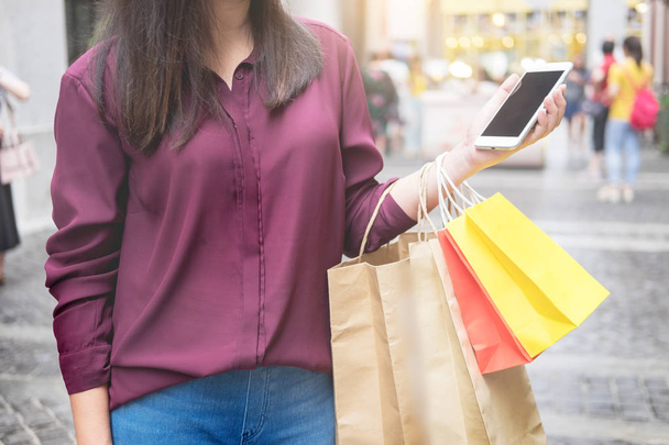 Mulher olhar para o telefone móvel com sacos de papel no shopping enquanto desfruta de um dia de compras
 - Foto, Imagem