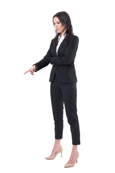 Mujer de negocios elegante serio en traje negro apuntando con el dedo hacia abajo y condescendiente. Cuerpo completo aislado sobre fondo blanco
.  - Foto, Imagen