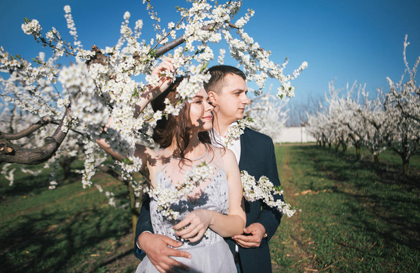 loving couple - the bride and groom in a light dress on a wedding walk in the flowering gardens in the spring, tender emotions - Φωτογραφία, εικόνα