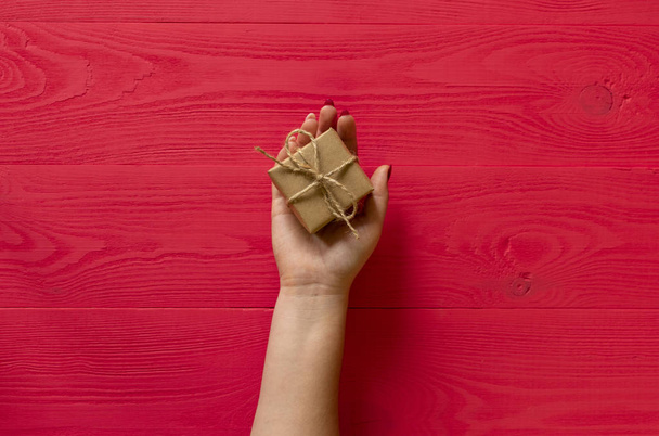 female hands give present on wooden red background - Фото, изображение