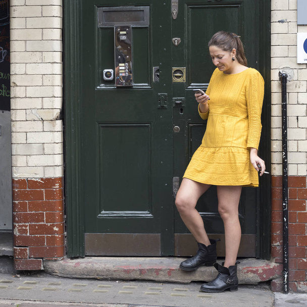 LONDON, ENGLAND - November 12, 2018 The girl in the yellow dress smokes at the green door - Photo, image