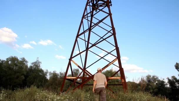 een man in grijze korte broek en een t-shirt komt tot een roestige pole-position voor elektriciteit en stijgt - Video