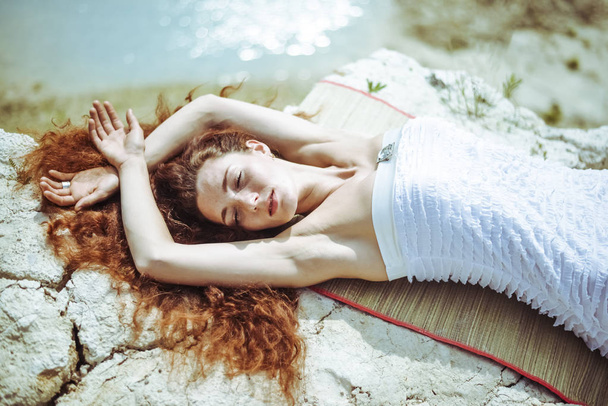 mujer vestida de blanco en la roca. Hermosa chica pelirroja está en la orilla del mar tropical
. - Foto, Imagen