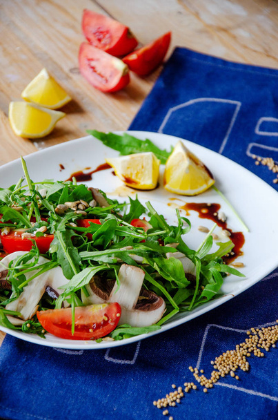 Свежий овощной салат с рукколой, грибами, помидорами в лимонно-медовом соусе на голубой салфетке. Концепция здорового питания. правильное питание
 - Фото, изображение