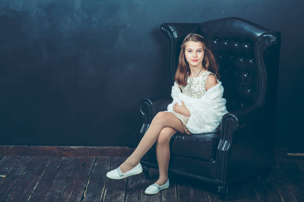 long-haired girl in a gray dress and a white Bolero sitting in a black leather chair - Fotoğraf, Görsel