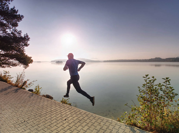 Man running on lake shore pavement during sunrise or sunset - healthy lifestyle concept - Photo, Image