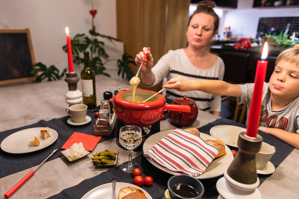 Fondue tradicional de queso suizo en una olla roja sobre mesa de comedor de hormigón
. - Foto, imagen