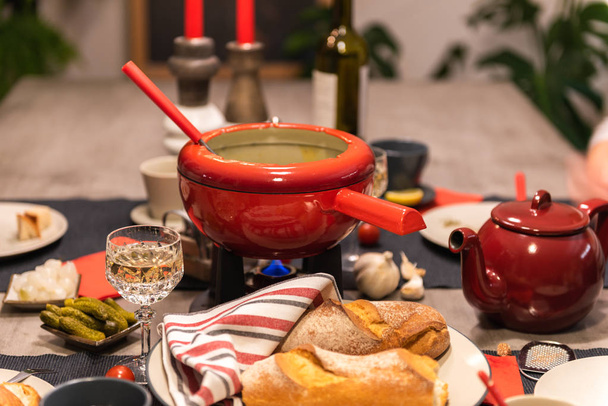 Παραδοσιακό fondue ελβετικών τυριών σε μια κόκκινη κατσαρόλα σε συγκεκριμένο τραπέζι φαγητού. - Φωτογραφία, εικόνα