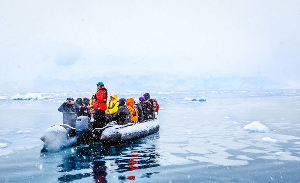 Schneefall über dem Boot mit gefrorenen Touristen, die zwischen Eisbergen treiben, nahe der antarktischen Halbinsel Almirante braun - Foto, Bild