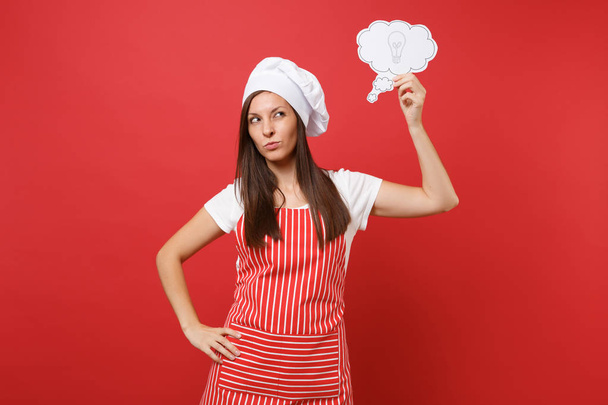 Hospodyňka žena kuchař kuchař nebo baker v pruhované zástěry bílé tričko toque šéfkuchaři klobouk izolované na pozadí červené zdi. Zamyšlená žena myslí, hold říkají cloud s myšlenkou žárovka. Vysmívat se koncepce prostoru kopie - Fotografie, Obrázek