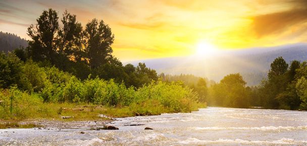 Яркий восход солнца в горах Карпат, Украина. Солнечные лучи отражаются в горной реке. Широкое фото
. - Фото, изображение