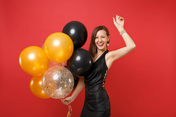 Lachen jonge vrouw in de kleine zwarte jurk vieren, stijgende hand, lucht ballonnen geïsoleerd op heldere rode achtergrond te houden. Concept vakantie feest van St. Valentine's Day, Happy New Year, verjaardag mockup - Foto, afbeelding