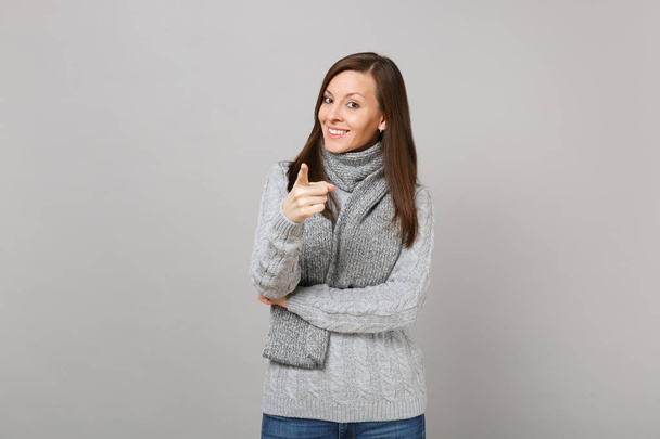 Улыбающаяся молодая женщина в сером свитере, шарф указывающий указательным пальцем на камеру изолирован на сером фоне стены. Здоровый образ жизни моды, люди искренние эмоции холодного сезона концепции. Пространство для копирования
 - Фото, изображение