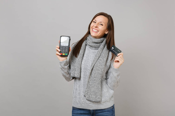 Красива жінка в светрі, шарф тримає бездротовий сучасний банківський платіжний термінал, щоб обробити, придбати кредитні карткові платежі ізольовані на сірому фоні. Стиль життя, люди щирі емоції, концепція холодного сезону
 - Фото, зображення