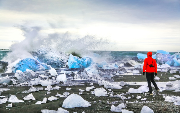 vrouw kijken golven crash tegen ijsbergen op jokulsarlon glaciale lagune, IJsland - Foto, afbeelding