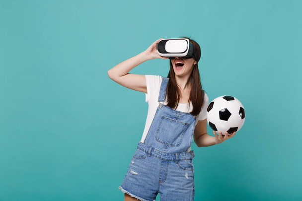 Cheerful young girl football fan looking in headset holding soccer ball playing isolated on blue turquoise wall background. People emotions, sport family leisure lifestyle concept. Mock up copy space - Photo, Image
