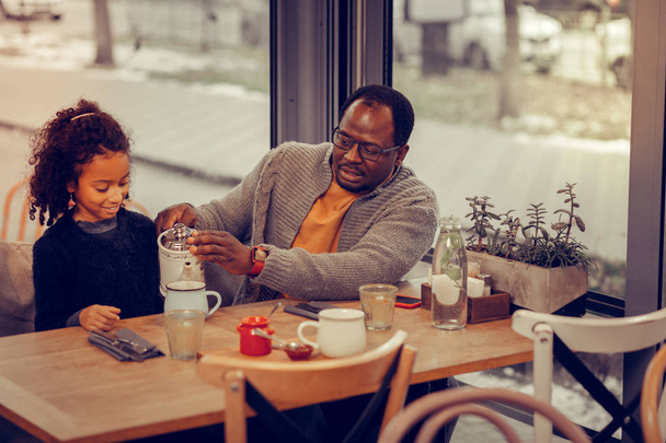 Loving father taking care of his daughter pouring hot tea for her - 写真・画像