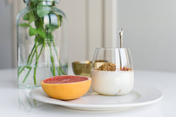 Healthy breakfast. Ingredients: grapefruit, granola, tea, lychee. Vase of roses. Side view, white background. - Fotoğraf, Görsel
