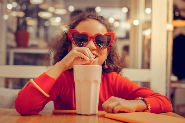 Curly appealing girl wearing bracelets enjoying her milkshake - Φωτογραφία, εικόνα