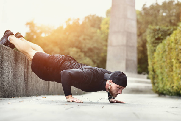 Young bearded sportsman makes workout in a park, doing a series of push ups outdoor. - Fotografie, Obrázek