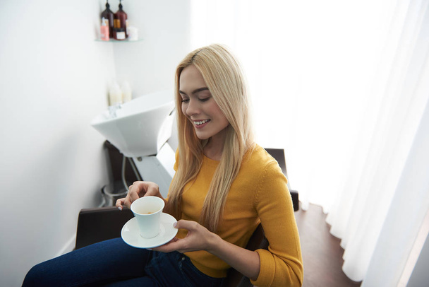 Beautiful young woman enjoying hot drink in beauty salon - Photo, image