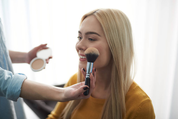 Skillful makeup artist applying powder on young lady face - Foto, Bild