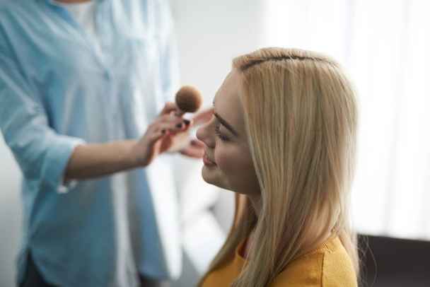 Artista de maquillaje talentoso aplicando polvo en la cara de dama
 - Foto, imagen
