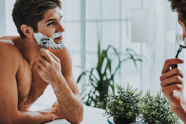 Smiling guy shaving his beard by razor - Zdjęcie, obraz