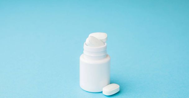 Close up pills spilling out of pill bottle on blue background. Medicine, medical insurance or pharmacy concept. - Valokuva, kuva